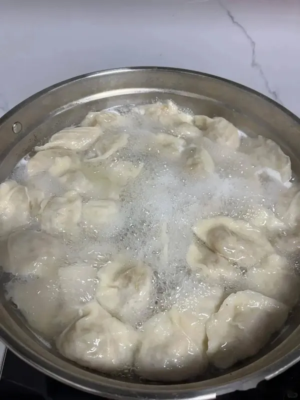 Boiling dumplings in a large pot, adding cold water